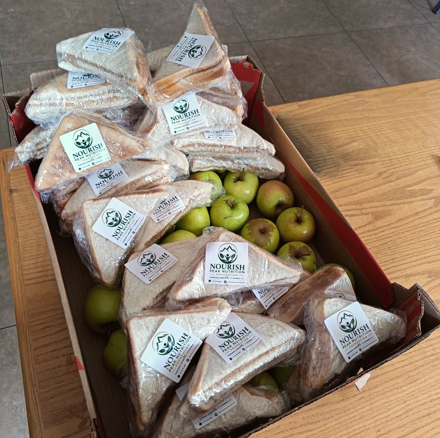 A box of individually wrapped Nourish Peak sandwiches and apples ready for distribution